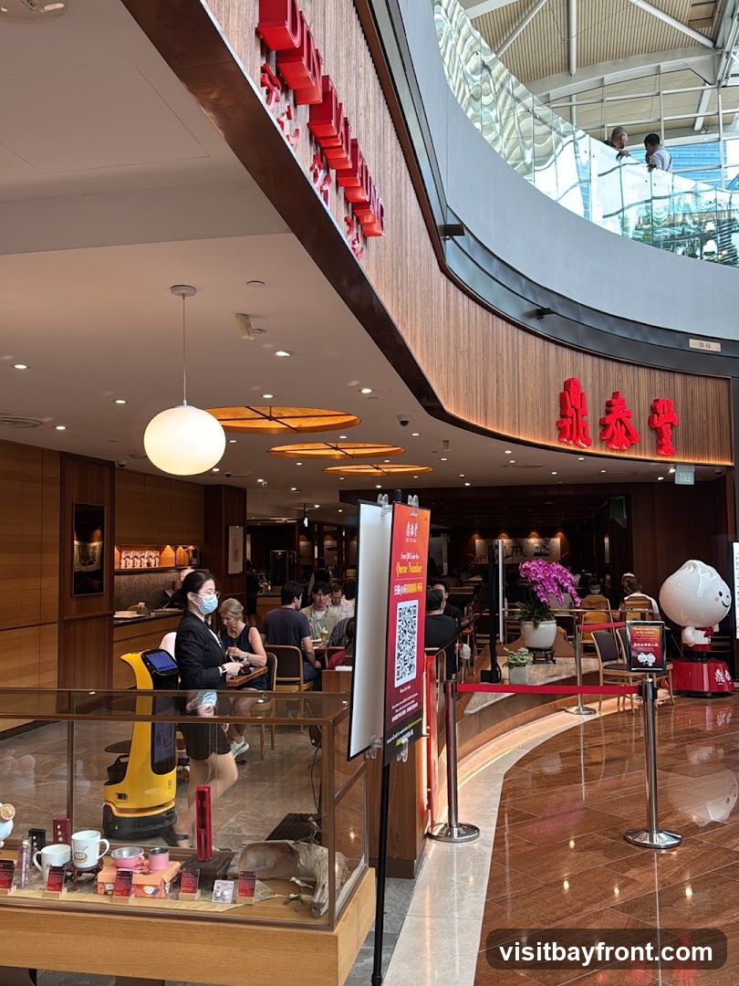 A view inside a restaurant with red Chinese characters on the wall. A queue sign with a QR code is visible, along with a mascot of a steamed bun. People are seated at tables, and a robot is present. A display case with merchandise is in the foreground.