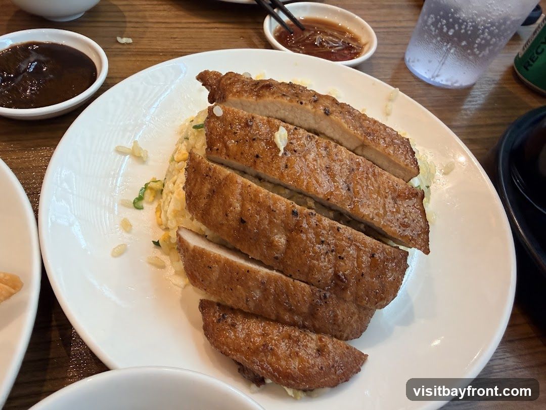 A close-up shot of a plate of fried rice topped with sliced grilled pork chops. There are two small dipping sauce bowls and a glass of water on the table.