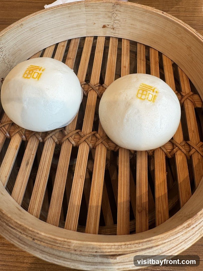 Two white steamed buns with a yellow symbol on top are presented in a bamboo steamer basket.