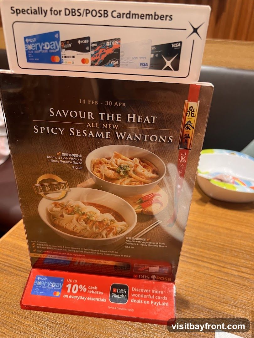 A promotional menu stand featuring "All New Spicy Sesame Wantons" with images of two dishes. It highlights a promotion for DBS/POSB Cardmembers offering up to 10% off. The menu also mentions that the dish contains nuts.
