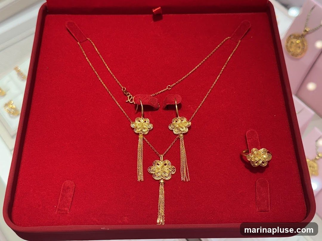 A gold necklace, earrings, and ring are displayed in a red velvet jewelry box. The jewelry features intricate knot designs with dangling chains. Other gold jewelry pieces are visible in the background.