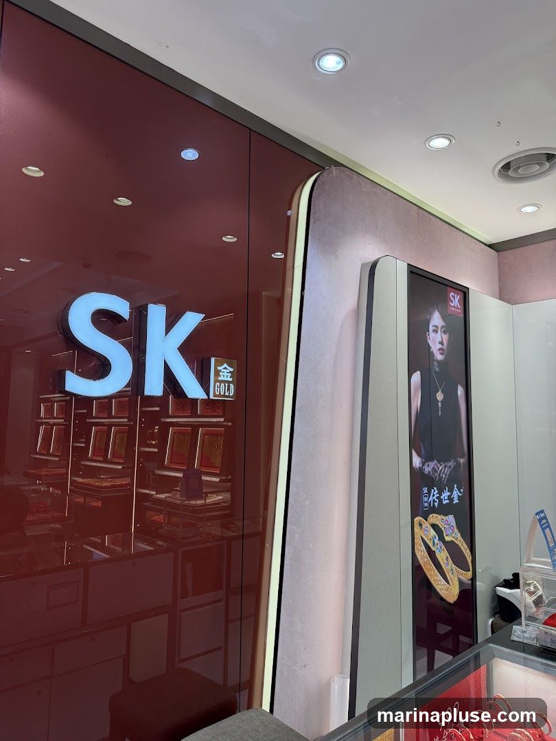 A display inside a jewelry store with the prominent "SK GOLD" logo. The store features glass display cases filled with gold jewelry, and a large vertical advertisement showcasing a model wearing jewelry and two ornate gold bracelets. The overall aesthetic is luxurious and modern.