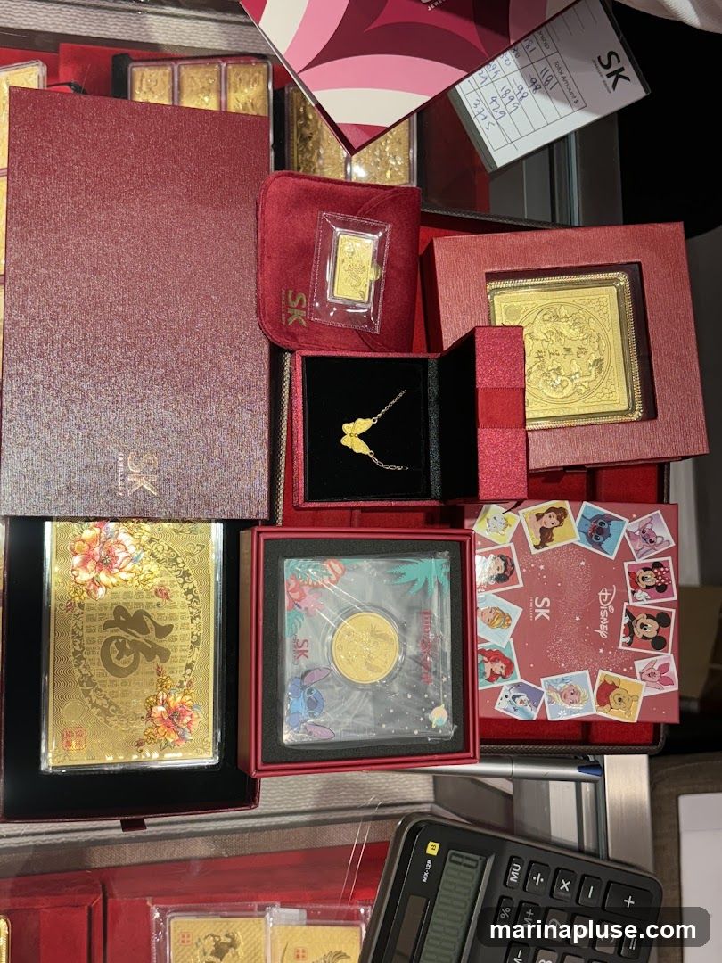 A collection of gold bars, a gold necklace, and gold coins are displayed in red and gold boxes. Some items feature intricate designs, while others are branded with Disney characters. A calculator and a receipt are also visible.