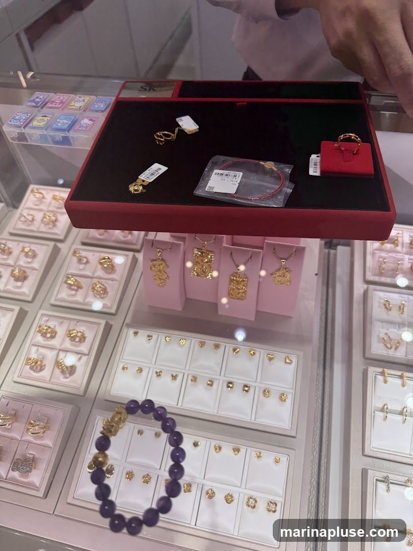 A display case filled with various gold jewelry, including rings, necklaces, and earrings. A purple beaded bracelet with a gold charm is in the foreground. Several small boxes with cartoon characters are visible on the left.
