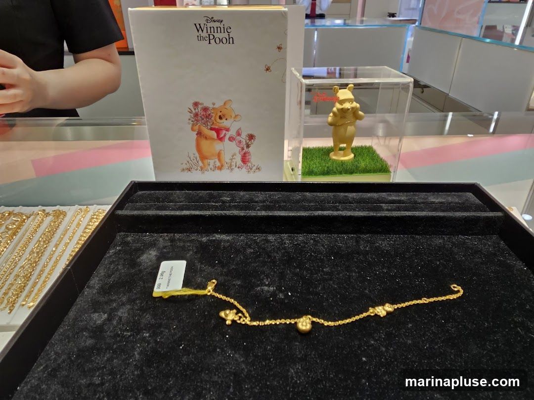 A display case shows gold jewelry, including a bracelet with small charms. A box with Winnie the Pooh and Piglet artwork is visible, along with a gold figurine of Winnie the Pooh in a clear case. The jewelry is presented on a black velvet tray.