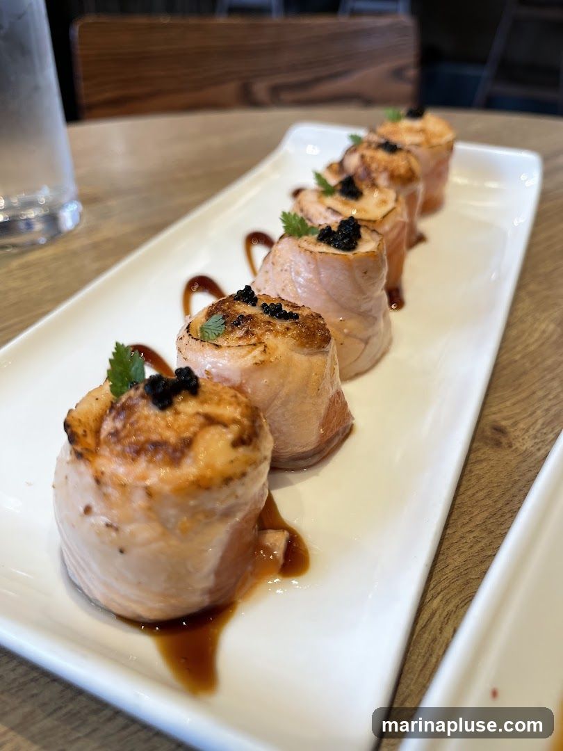 A white rectangular plate holds six seared salmon rolls, each topped with black caviar and a sprig of parsley. The rolls are arranged in a line, with a drizzle of dark sauce on the plate. A glass of water and a wooden table are visible in the background.