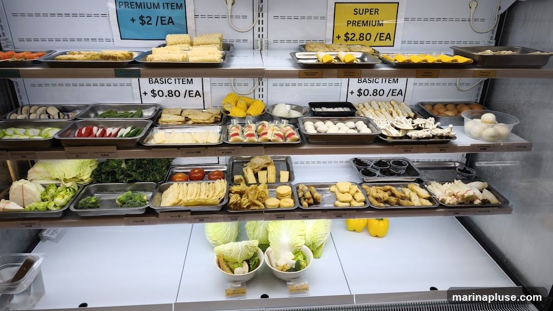 A refrigerated display case filled with various food items, including vegetables, tofu, mushrooms, and processed food. Price labels indicate different tiers: Premium Item at $2/EA, Basic Item at $0.80/EA, and Super Premium at $2.80/EA.
