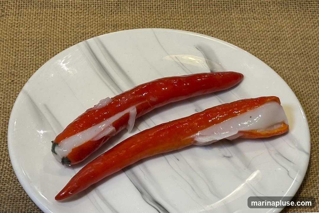 Two imitation crab sticks are presented on a white plate with a marble pattern. The crab sticks have a bright orange-red exterior and a white, flaky interior. The plate is set on a textured brown surface, possibly burlap.