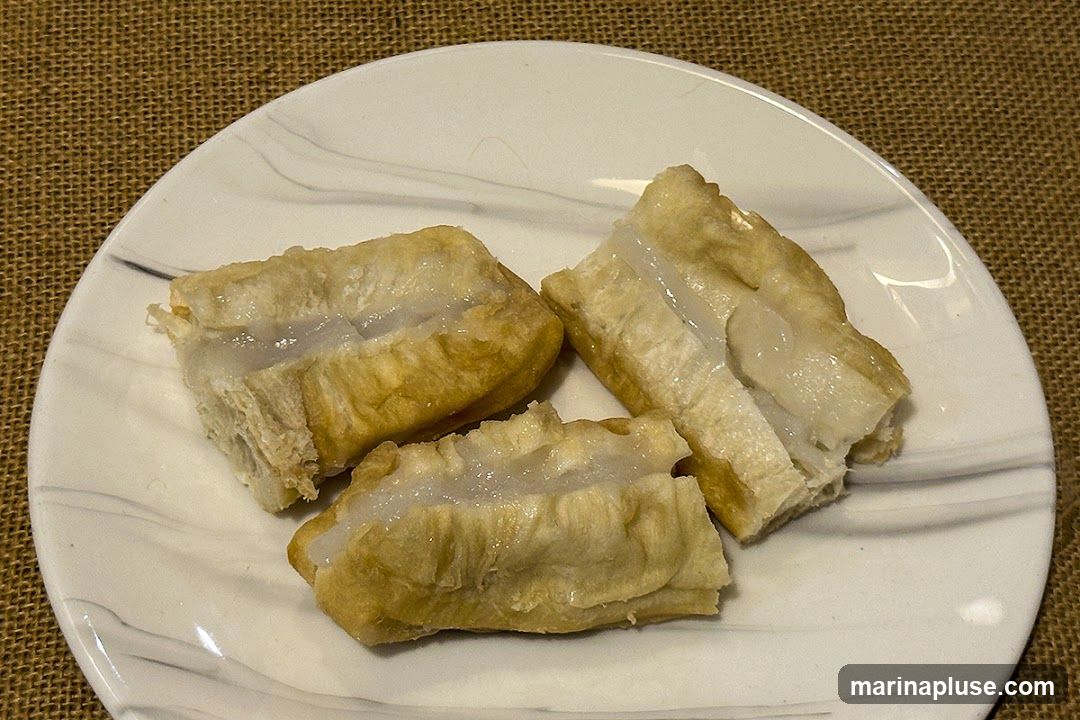 Three pieces of fried dough, cut open to reveal a white, creamy filling, are arranged on a white plate with a marbled pattern. The plate rests on a textured brown surface.