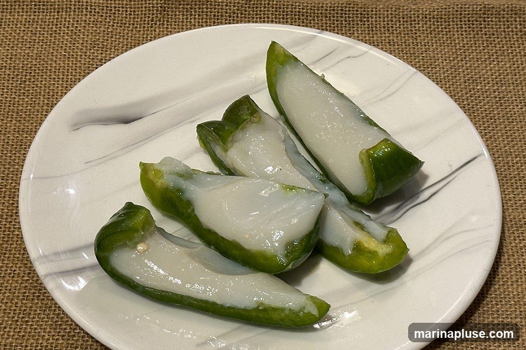 Four pieces of green pepper stuffed with a white, creamy filling, served on a white plate with gray marbling. The plate is set on a burlap-like surface.