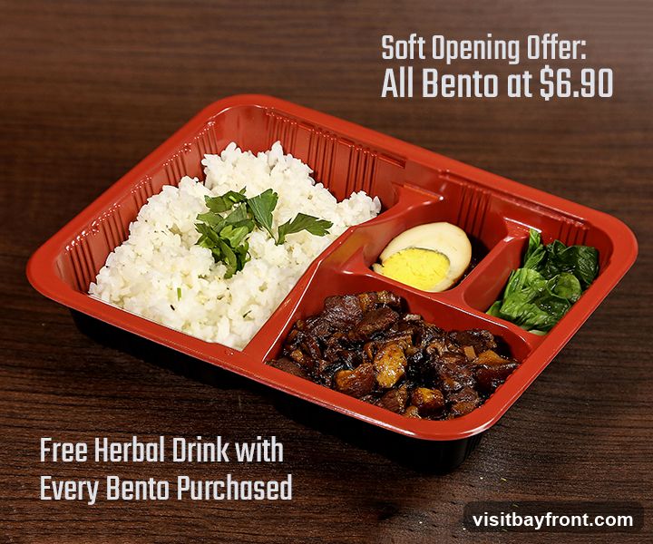 A bento box with rice, braised meat, a hard-boiled egg, and greens. The image advertises a soft opening offer of all bento boxes at $6.90 and a free herbal drink with every bento purchased.
