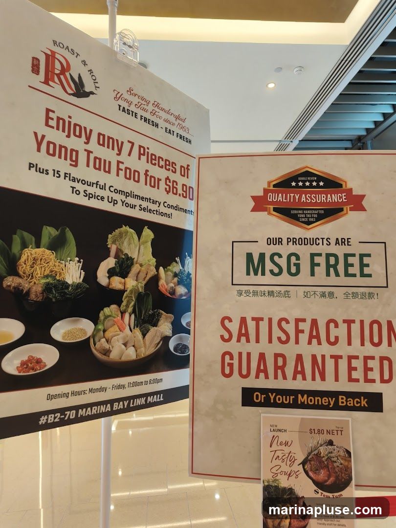 Two large posters are displayed. The left poster advertises a deal for 7 pieces of Yong Tau Foo for $6.90, plus 15 complimentary condiments. It also shows images of the ingredients and lists opening hours and the mall location. The right poster highlights that their products are MSG-free and offers a satisfaction guarantee. It also promotes a new launch of "Tasty Soups" with a Tom Yum option for a $1.80 top-up.