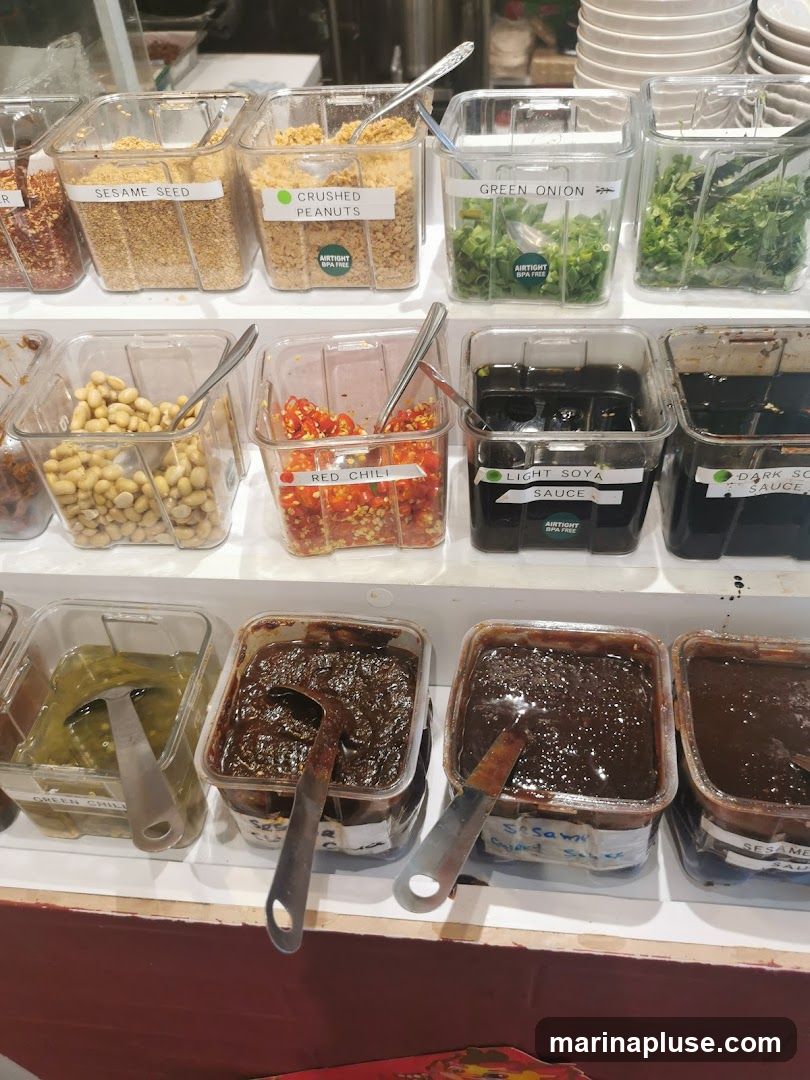 A selection of condiments in clear plastic containers, including sesame seeds, crushed peanuts, green onions, red chilies, light soy sauce, dark soy sauce, and various sauces.