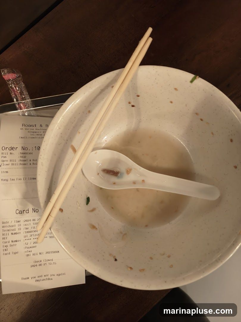An empty bowl with leftover broth and a spoon and chopsticks resting on it. A receipt is placed next to the bowl. The receipt shows details of an order from "Roast & R" and payment information.
