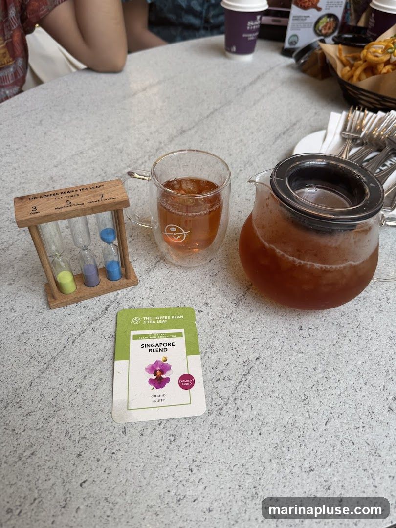 A table setting with a glass of iced tea, a teapot of tea, and a tea timer. A card for "Singapore Blend" tea is also visible.