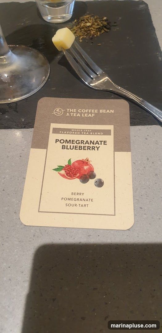 A card from The Coffee Bean & Tea Leaf advertising their Pomegranate Blueberry whole leaf flavored tea blend. The card features an illustration of a pomegranate and blueberries, with descriptive text below.