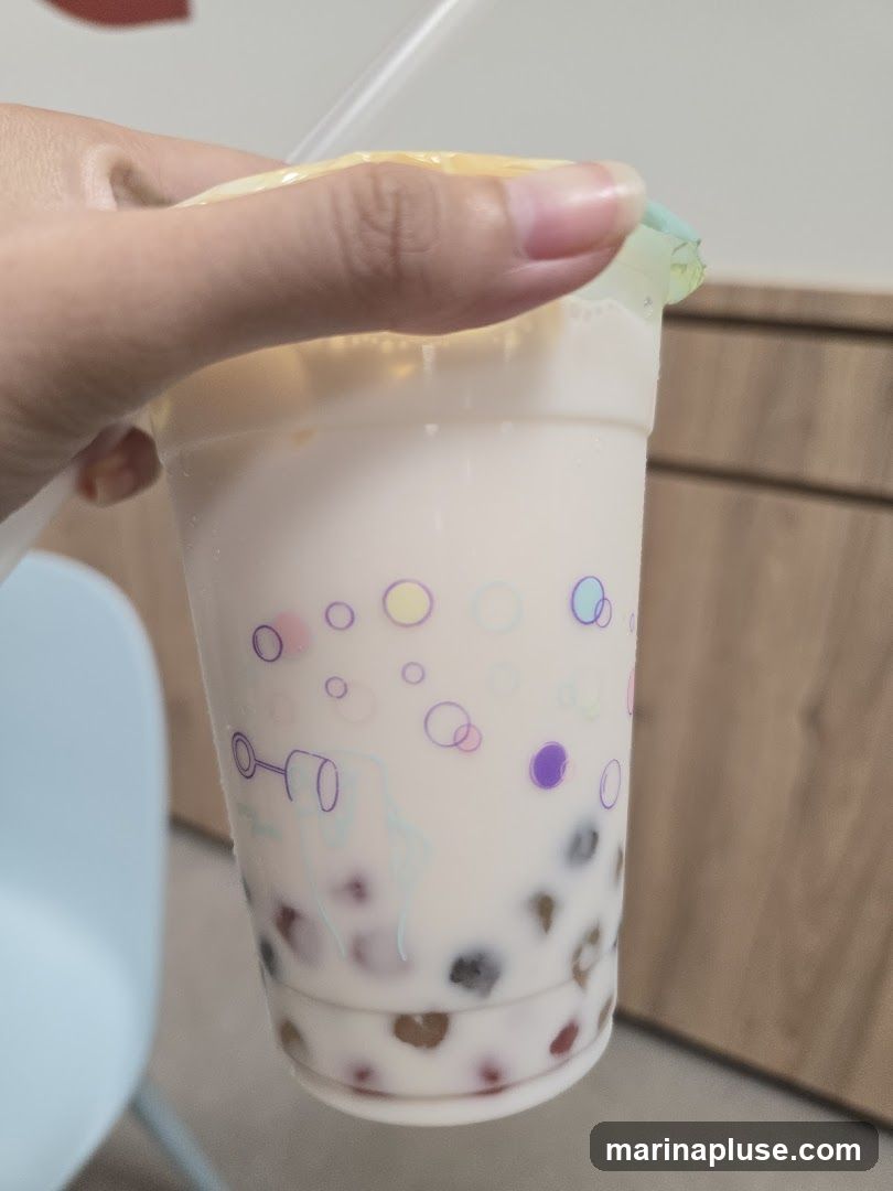 A hand holds a plastic cup filled with a milky beverage and tapioca pearls. The cup has a colorful bubble design printed on it.