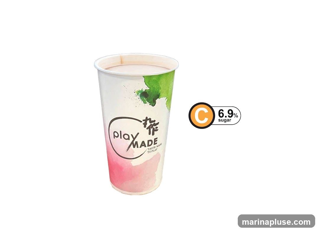 A paper cup with a watercolor design of pink and green splashes. The cup has a black oval logo with the text "play MADE" and smaller text below that reads "TASTE MADE TO PLAY". To the right of the cup is a circular orange and black label with the letter "C" inside the circle and the text "6.9% sugar" next to it. The cup appears to contain a light-colored beverage.