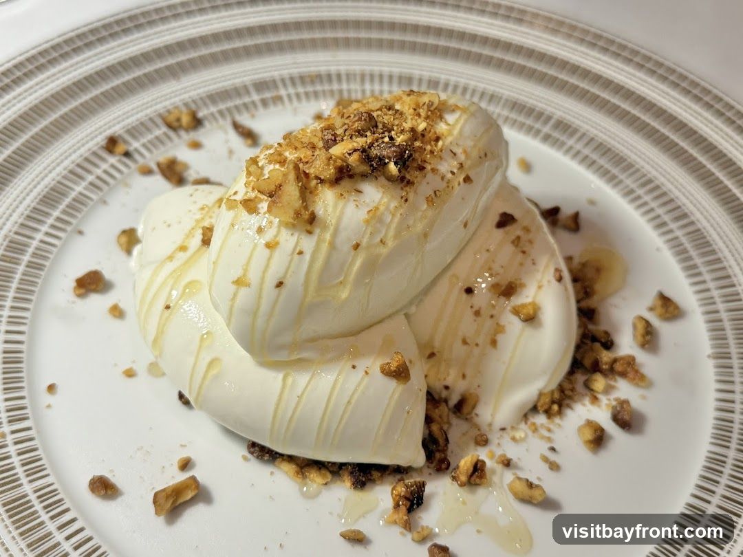 A close-up shot of a white dessert, possibly yogurt or ice cream, topped with chopped nuts and drizzled with honey. The dessert is served on a white plate with a decorative rim.