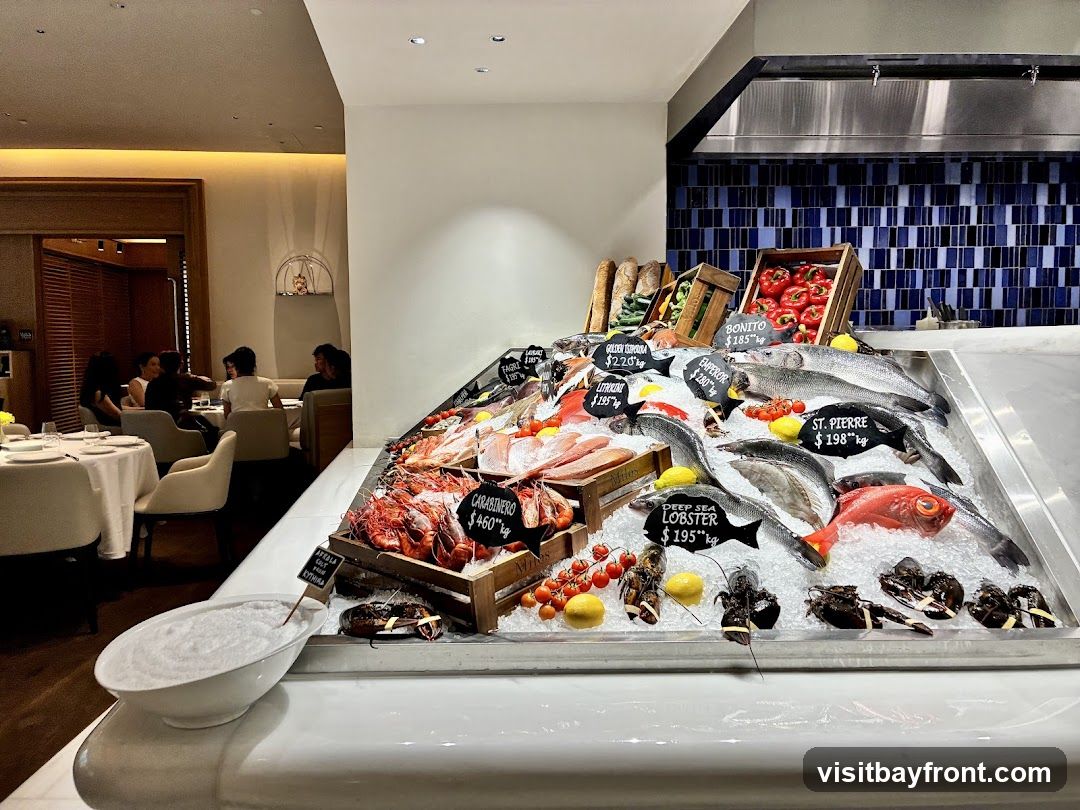 A display of fresh seafood on ice, including various fish, lobsters, and prawns. Price tags are visible for some items. In the background, diners are seated at tables in a restaurant setting.