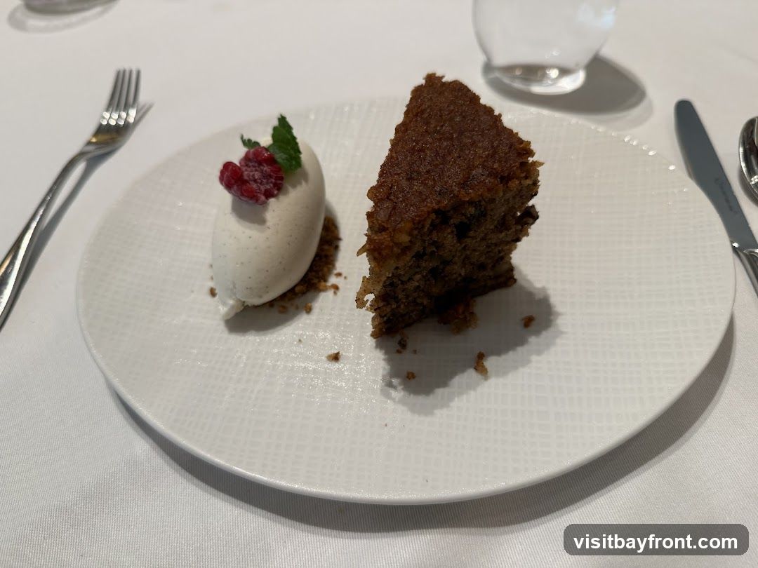 A slice of cake with a scoop of ice cream and a raspberry on a white plate.