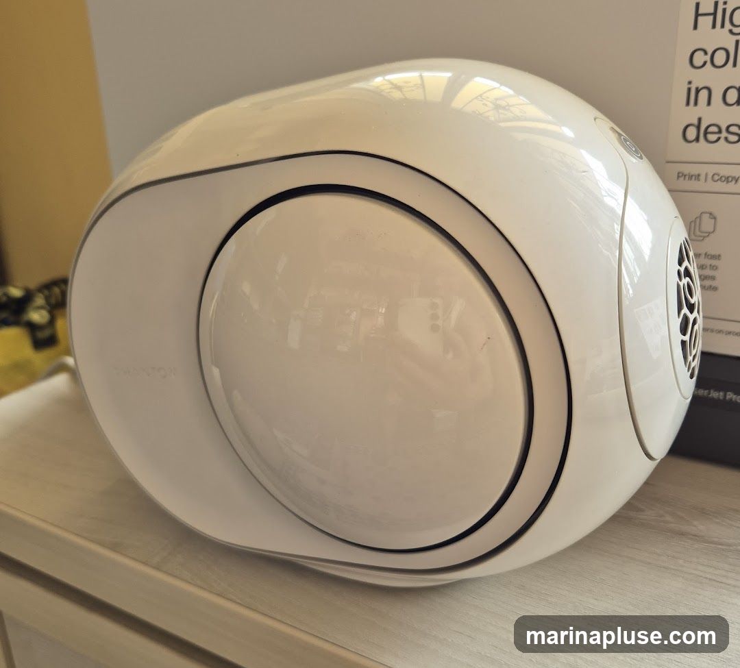 A white, ovular speaker with a spherical element in the center. The word "PHANTOM" is visible on the side of the speaker. A box with text is in the background.