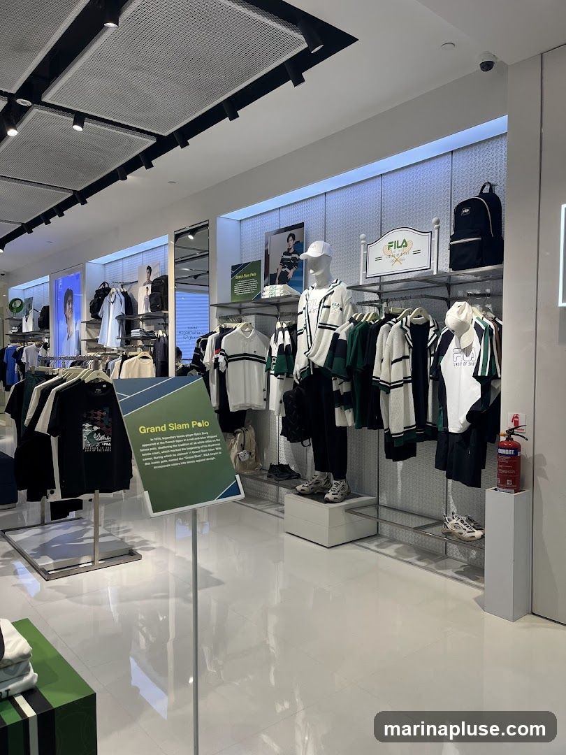 The interior of a Fila store displays clothing and accessories on racks and mannequins. A sign describes the "Grand Slam Polo." The store has a clean, modern aesthetic with white walls and polished floors.
