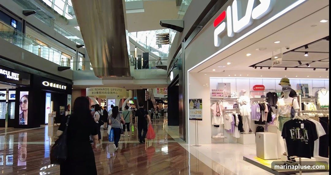 The interior of a Fila store with clothing displayed on mannequins and racks. The Fila logo is visible above the entrance. Other stores, including Oakley and Miracle Hut Boutique, are visible in the background within a shopping mall.