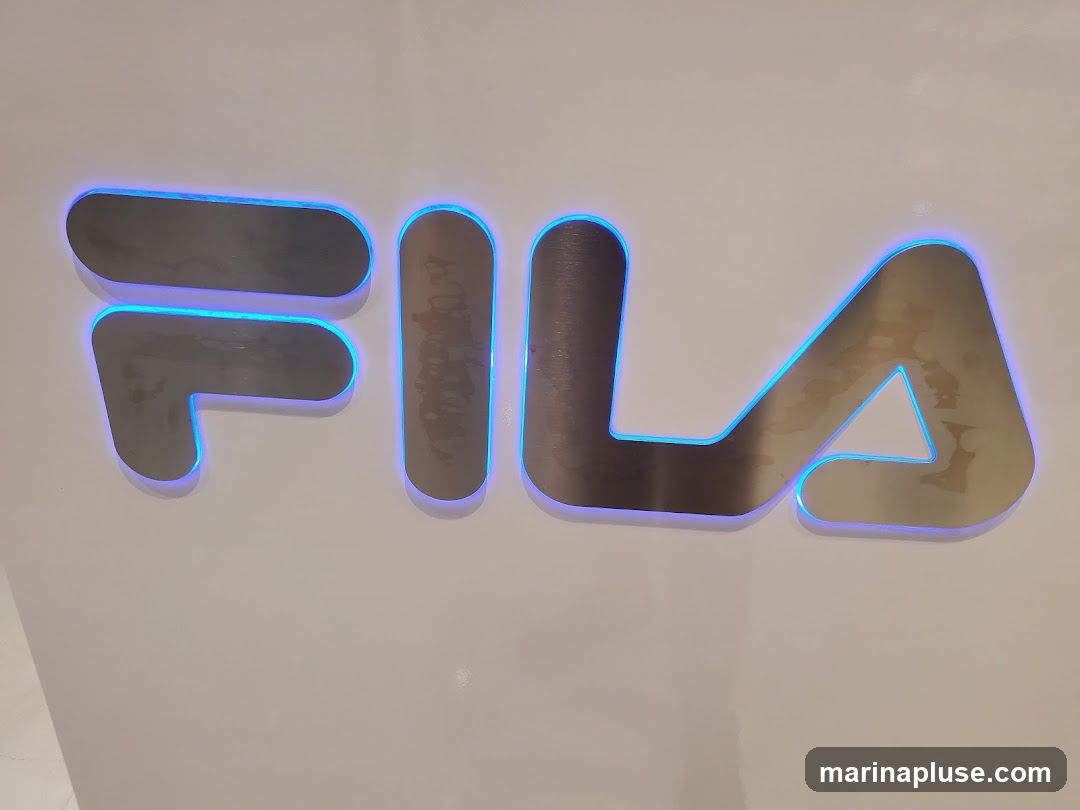 A close-up shot of the Fila logo, with the letters illuminated by a blue neon glow. The logo is mounted on a white surface.