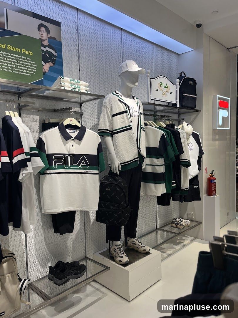 A Fila store display featuring mannequins, clothing, backpacks, and shoes. A poster on the left advertises a "Grand Slam Polo" inspired by tennis player Björn Borg. The store has a clean, modern aesthetic with white walls and metal shelving.