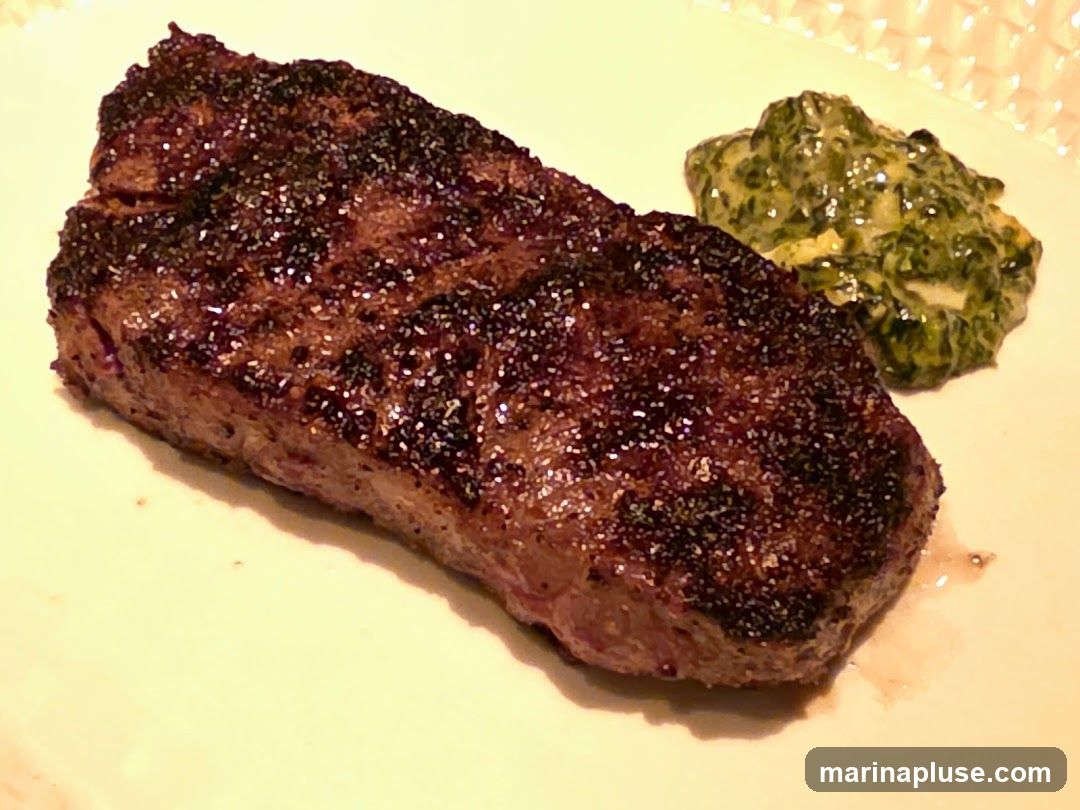 A close-up shot of a grilled steak served with a side of creamed spinach. The steak is seasoned with coarse salt and pepper, giving it a dark, crusted exterior. The creamed spinach appears rich and creamy, with visible pieces of spinach.