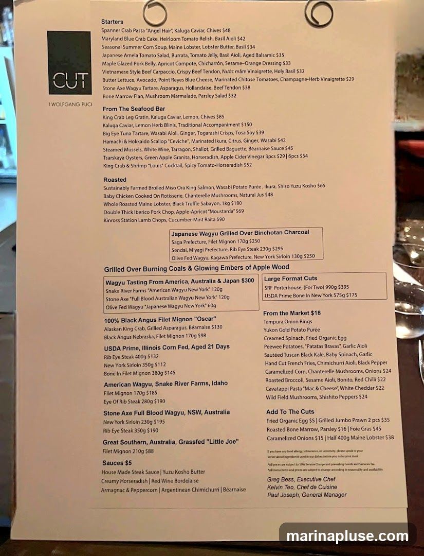 A menu from CUT by Wolfgang Puck, featuring starters, seafood, roasted dishes, various cuts of Wagyu and Angus beef, and sauces.