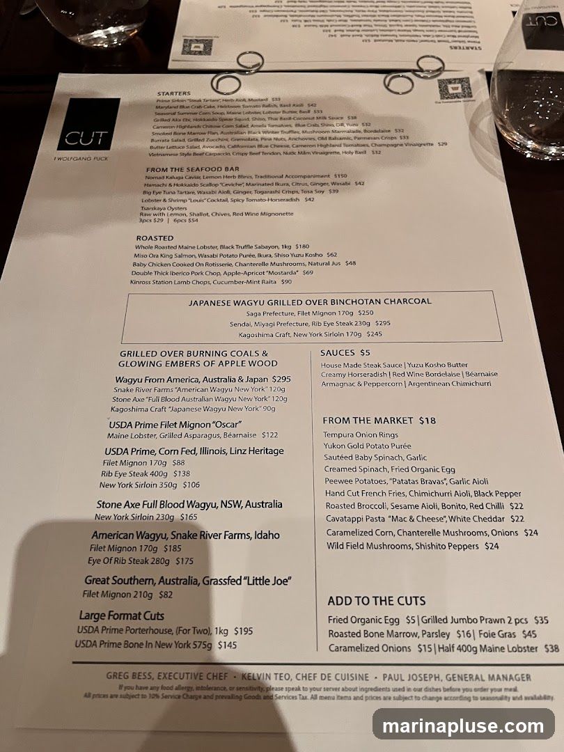 A menu from CUT by Wolfgang Puck, featuring starters, seafood, roasted dishes, Japanese Wagyu, and various cuts of steak.