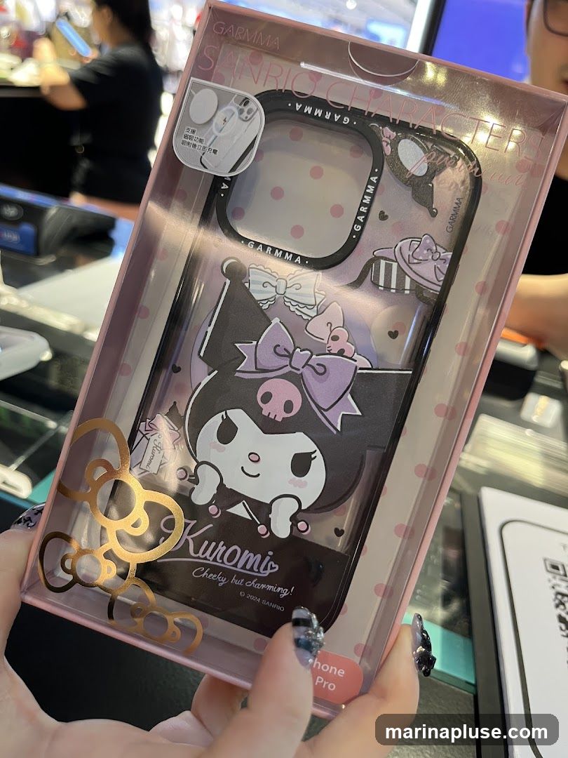 A person is holding a clear plastic package containing an iPhone case featuring the Sanrio character Kuromi. The case is black with purple accents and has Kuromi's image prominently displayed. The packaging also shows the "Garrma" and "Sanrio Characters" branding. The background appears to be a retail store setting.