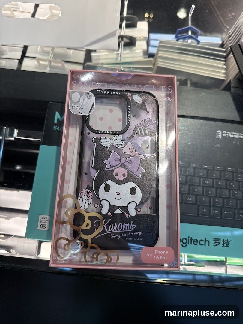 A packaged iPhone case featuring the Sanrio character Kuromi. The packaging also indicates it is for the iPhone 16 Pro and is made with 60% recycled plastic. Other electronic accessories are visible in the background.