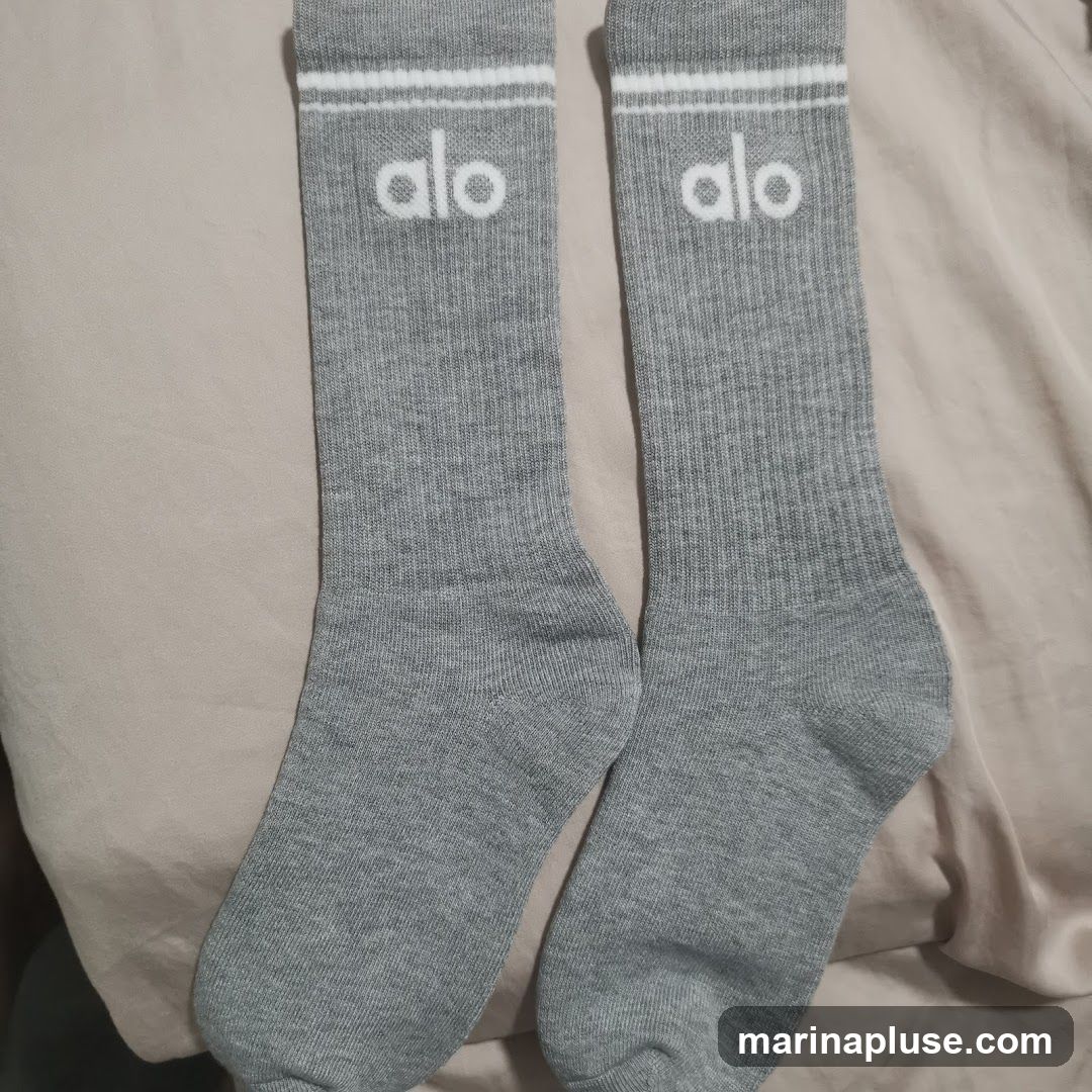 A pair of gray crew socks with white stripes at the top and the white 'alo' logo printed below the stripes.