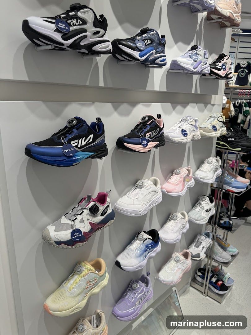 A wall display of various Fila brand sneakers in different colors and styles. The shoes are mounted on white shelves. Some shoes have 'New Arrival' tags. In the background, more shoes and apparel are visible on shelves.
