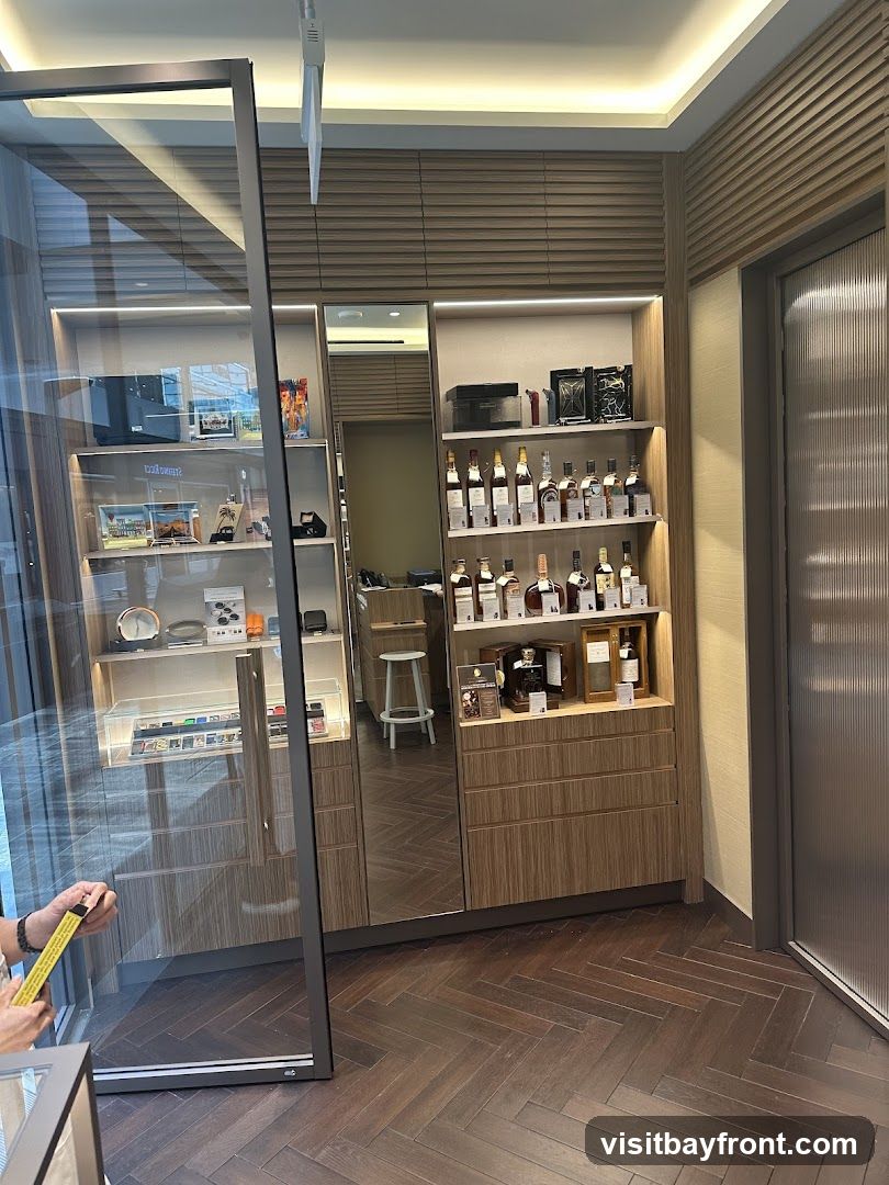 The image shows the interior of a store with wooden floors and walls. There are display shelves filled with bottles, likely spirits, and various other items. A large mirror reflects a stool and more shelving. A glass display case is visible on the left.