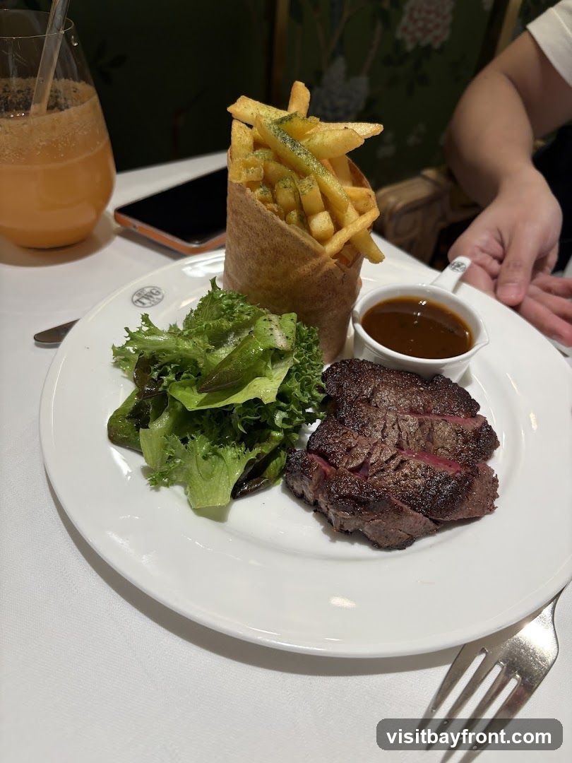 A plate of steak, fries, and salad is served with a side of sauce. A glass of orange juice is visible in the background.