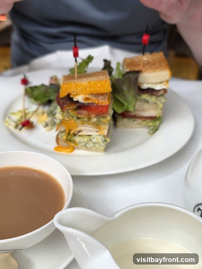 Two tall club sandwiches are served on a white plate with a side of salad. A cup of tea and a creamer are also on the table.