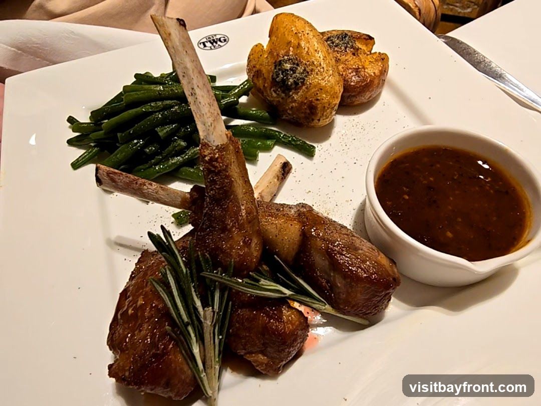 A plate of lamb chops served with roasted potatoes, green beans, and a side of sauce. The plate has a TWG Tea logo.