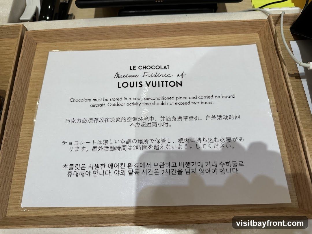 A sign with instructions on how to store and transport Louis Vuitton chocolate. The instructions are provided in English, Chinese, Japanese, and Korean. It states that chocolate must be stored in a cool, air-conditioned place and carried on board aircraft, with outdoor activity time not exceeding two hours.
