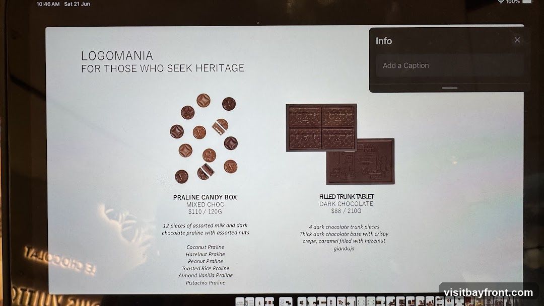 A presentation slide titled "LOGOMANIA FOR THOSE WHO SEEK HERITAGE" displays two chocolate products. On the left is a "PRALINE CANDY BOX" with 12 pieces of assorted milk and dark chocolate pralines with nuts, including Coconut, Hazelnut, Peanut, Toasted Rice, Almond Vanilla, and Pistachio Praline. It costs $110 for 120g. On the right is a "FILLED TRUNK TABLET DARK CHOCOLATE" with 4 dark chocolate trunk pieces, featuring a thick dark chocolate base with crispy crepe and caramel filled with hazelnut gianduja. It costs $88 for 210g.