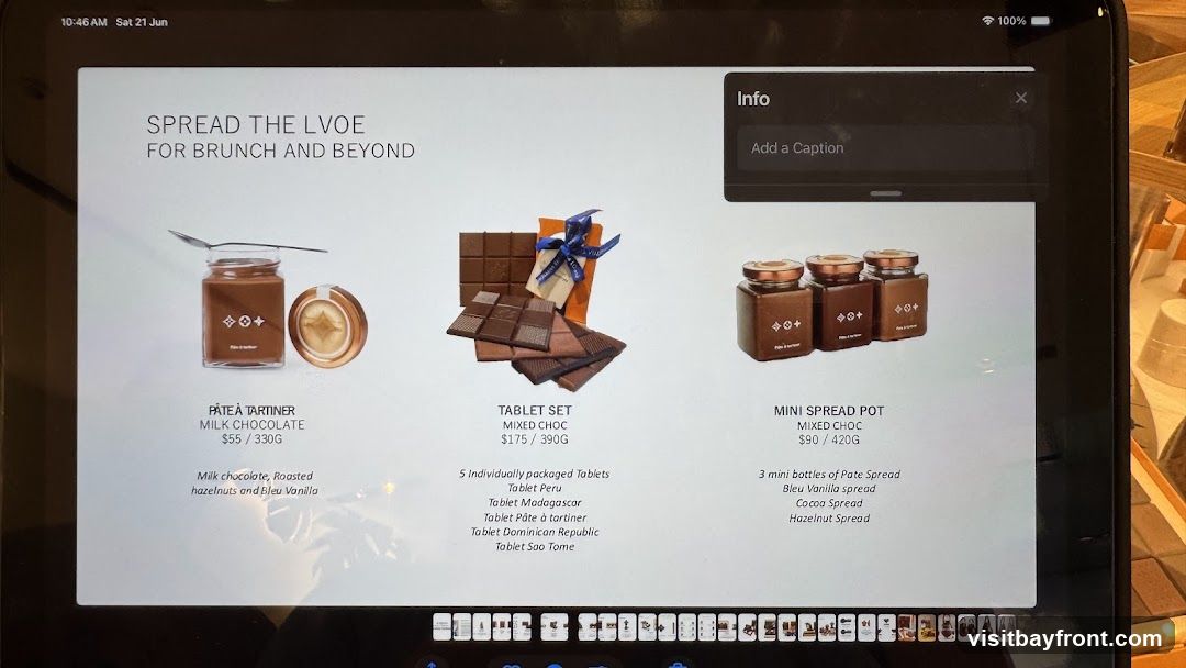 A digital display showcasing chocolate products. The display features three items: Pâte à Tartiner (Milk Chocolate Spread), a Tablet Set (Mixed Chocolate), and Mini Spread Pots (Mixed Chocolate). Each item has a description and price. The text "SPREAD THE LVOE FOR BRUNCH AND BEYOND" is prominently displayed at the top. An "Info" box with a caption field is visible in the upper right corner.