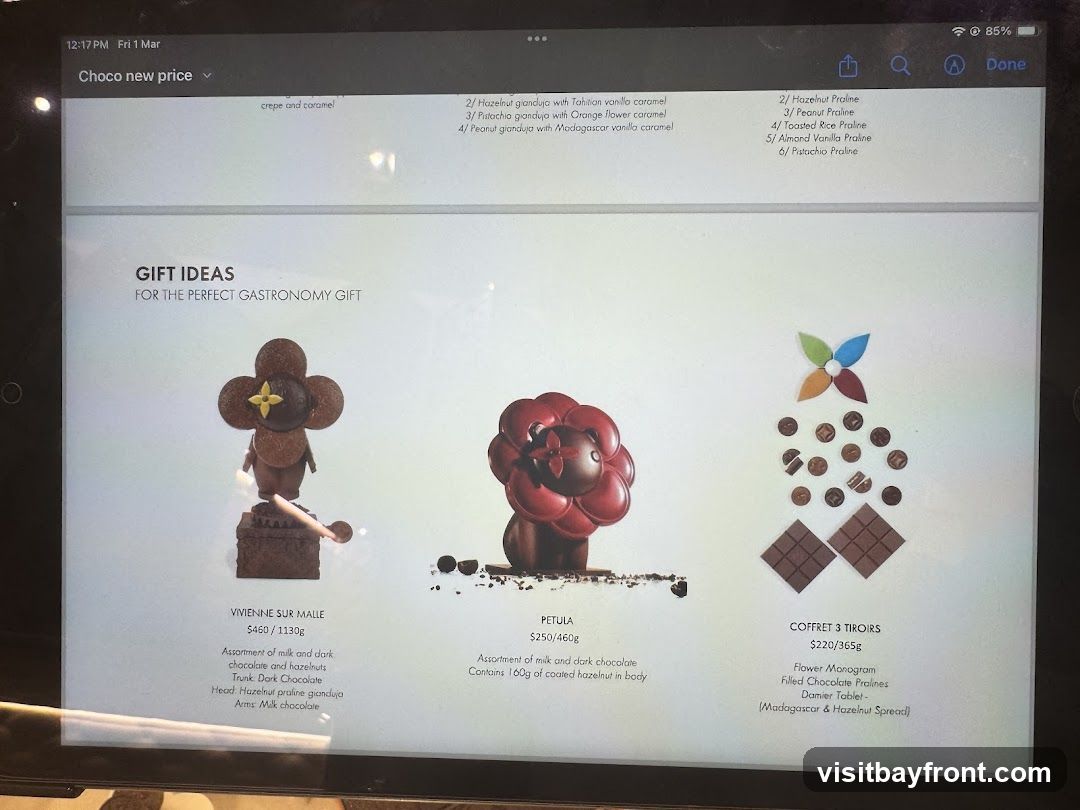 A digital display showcasing three chocolate gift sets: Vivienne Sur Malle, Petula, and Coffret 3 Tiroirs. Each item is accompanied by a description, weight, and price. A list of praline flavors is also visible.