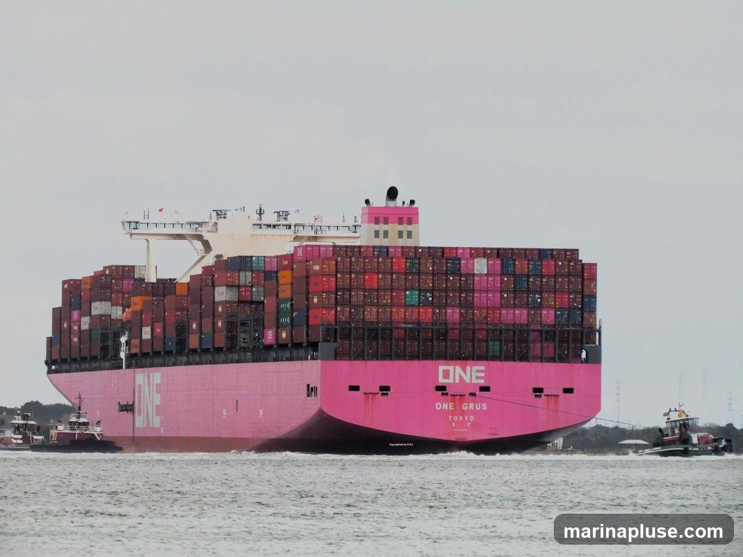 A large pink container ship named "ONE GRUS TOKYO" is being assisted by two tugboats in the water. The ship is laden with numerous colorful shipping containers stacked high. The sky is overcast.
