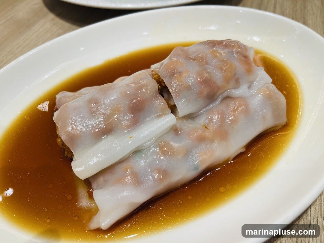 A close-up shot of steamed rice rolls served in a white oval dish with a savory brown sauce. The translucent rice noodle wrappers reveal a filling of minced meat and other ingredients. The dish appears to be a popular dim sum item.