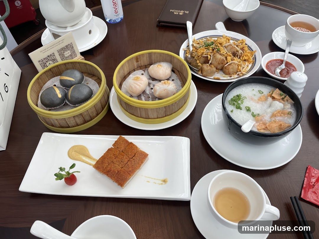 A table laden with various dim sum dishes, including steamed buns, dumplings, congee, crispy pork, and fried taro cakes. A bottle of Evian water and cups of tea are also visible.
