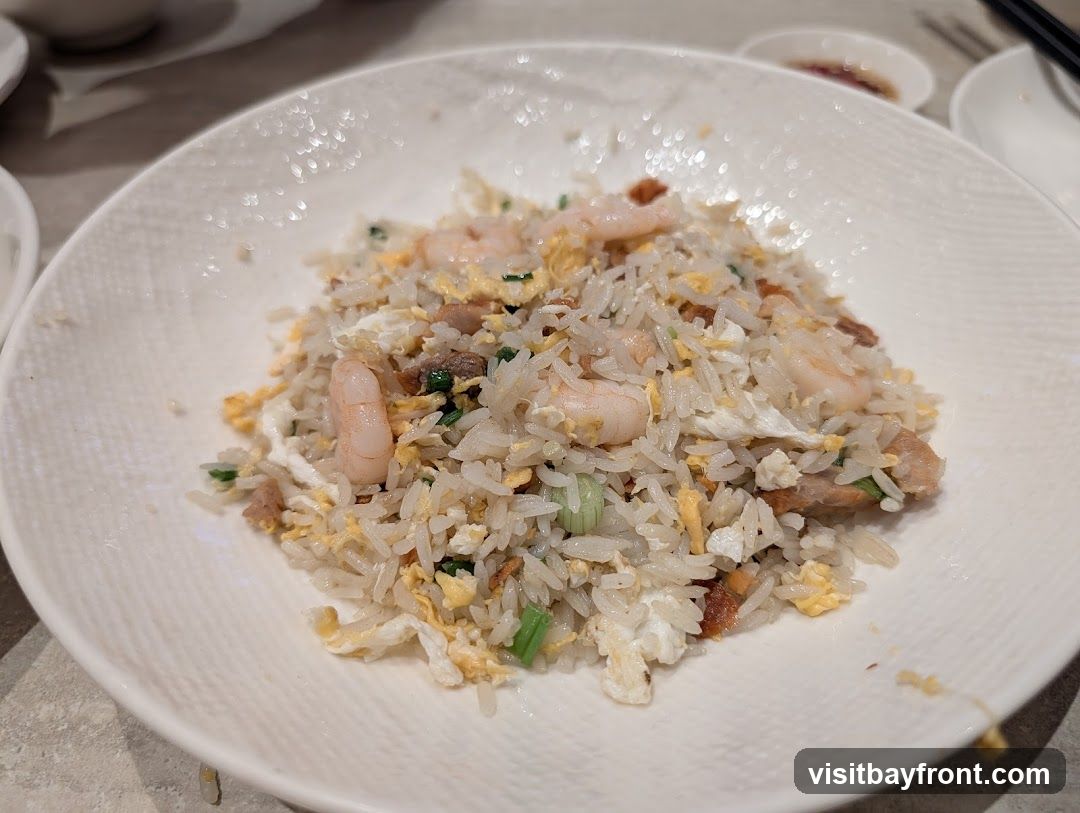 A close-up shot of a plate of shrimp fried rice. The rice is mixed with scrambled eggs, pieces of pork, and green onions. Several shrimp are visible throughout the dish. The plate has a textured rim.