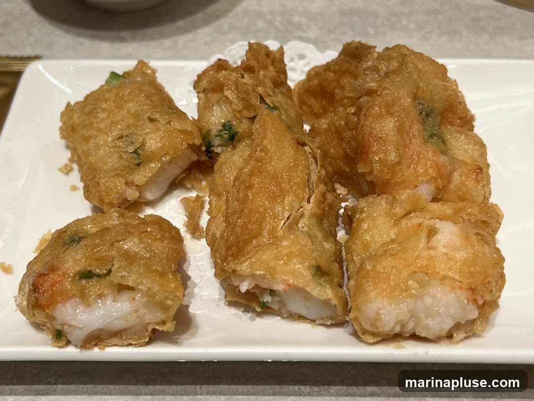 A close-up shot of several golden-brown fried shrimp rolls served on a white plate with a doily. The rolls are crispy and appear to be filled with shrimp and green onions.